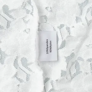 Detail des Stoffetiketts mit 90% Nylon und 10% Elasthan auf weißem floralem Spitzenrock
