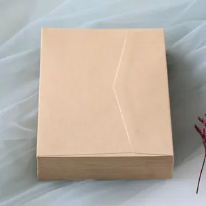 Stack of thick brown kraft paper envelopes on soft mesh fabric with dried floral accents