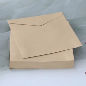 Close-up of stacked square kraft paper envelopes with natural texture on a soft fabric