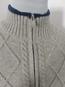 Makroaufnahme einer grauen Strickjacke mit Rautenmuster und metallischem Reißverschluss