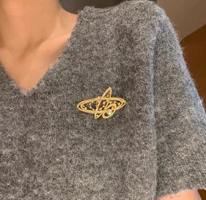 Gros plan d'une broche Saturne dorée avec perle blanche sur un pull en maille grise