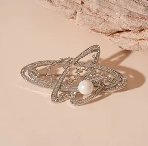 Détail d'une broche Saturne argentée avec zircons, étoiles étincelantes et perle centrale