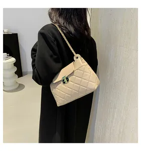 Sac à bandoulière beige matelassé avec chaîne dorée sur manteau noir pour look tendance