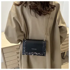 Détail du sac bandoulière léopard avec chaîne dorée sur fond de manteau beige élégant