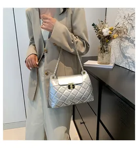 Détail d'un sac à bandoulière argenté matelassé avec fermoir doré et chaîne tressée