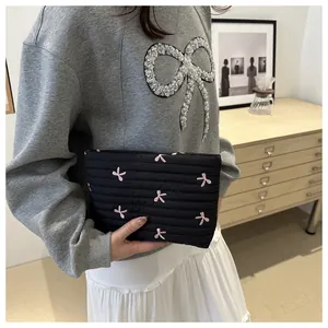 Detail of black quilted pouch with pink butterfly embroidery held by a model