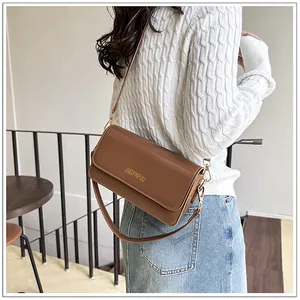 Close-up of a brown leather shoulder bag with gold hardware and flap closure on a model