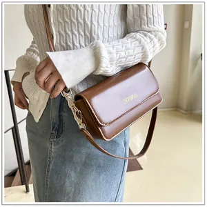 Detail view of a vintage brown leather crossbody bag with golden branding on model