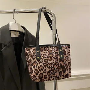 Detail of leopard print tote bag featuring black slim straps and golden rivet accents