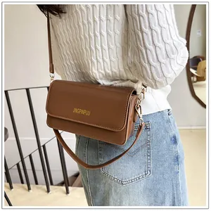 Close-up of a brown matte leather crossbody bag with gold lettering on a female model