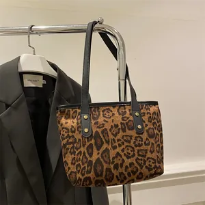 Detail of leopard print tote bag featuring black leather straps and gold rivet accents