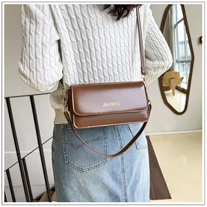 Detail of dark brown leather crossbody bag featuring gold logo and metallic hardware