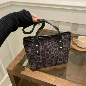 Detail of leopard print tote bag with black leather handles and gold rivet accents