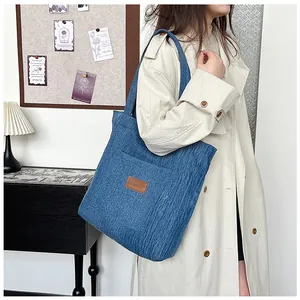Détail du sac cabas en jean bleu avec patch cuir sur mannequin en trench-coat