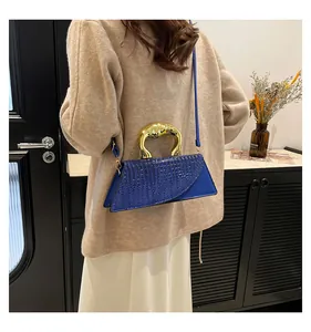 Detail of navy crocodile texture handbag with arched gold handle on a beige knit sweater