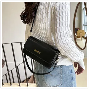 Detail of a black glossy leather baguette bag worn over the shoulder with gold lettering