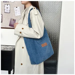 Détail du sac cabas en denim montrant la texture verticale et l'étiquette en cuir brun