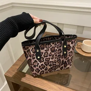 Detail of leopard print tote bag with black handles and decorative gold rivets