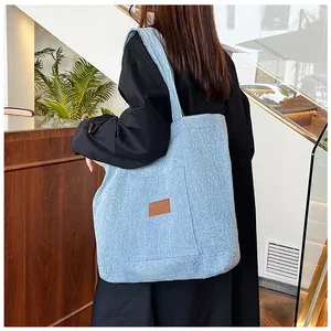 Détail du sac cabas en denim bleu clair avec étiquette en cuir et poche latérale