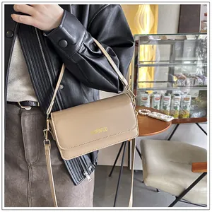Detailed close-up of beige leather shoulder bag with gold lettering and flap design