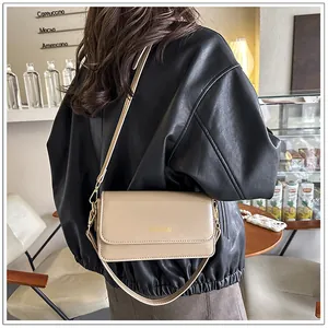 Detail of beige faux leather crossbody bag worn with a black jacket in a cafe setting