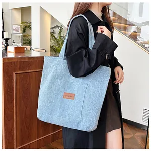 Détail du sac fourre-tout en jean bleu clair avec poche frontale et écusson de marque en cuir