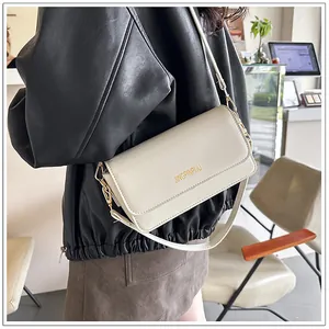 Chic beige leather crossbody bag with gold lettering shown on a model in a casual outfit