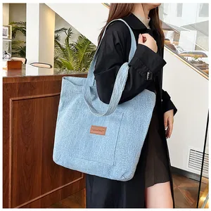 Détail du sac cabas en denim bleu avec logo en cuir marron et poche frontale