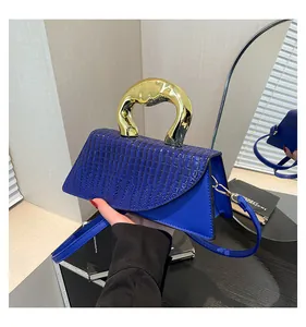 Detail of blue faux crocodile leather bag featuring a large gold circular metal handle