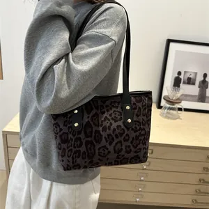 Shoulder view of a leopard print tote bag with black leather straps and gold rivets
