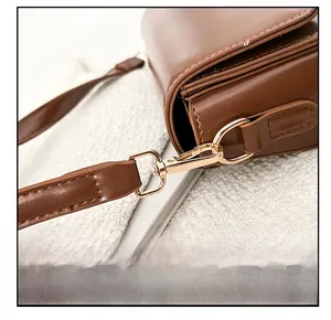 Detail of light gold metal hook and fine edge stitching on brown leather shoulder bag