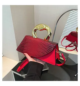 Detail of red croc-embossed handbag featuring a gold U-shaped handle and mirror reflection