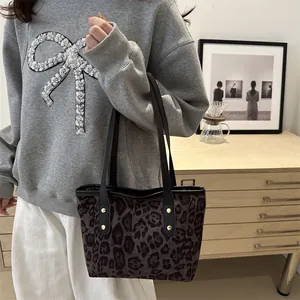 Close-up of leopard print tote bag featuring black shoulder straps and gold rivet details