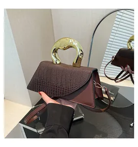 Close-up of brown crocodile pattern handbag with unique golden sculptural metal handle