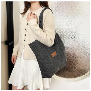 Détail du grand sac cabas en toile gris foncé avec un écusson logo en cuir marron