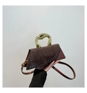 Detail of dark brown crocodile pattern bag with gold metal handle held by model