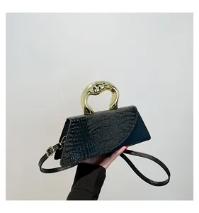 Detail of crocodile embossed leather handbag with arched gold metal handle and strap