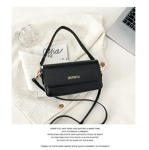 Detail of black rectangular flap bag with gold lettering and metallic side accents