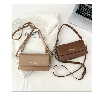 Close-up of khaki and brown flap bags with golden logo and adjustable straps on white coat