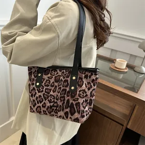 Detail of leopard print tote bag with black leather straps and gold rivets on a model