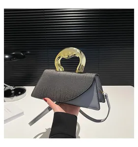 Detailed close-up of the textured grey flap and artistic golden metal handle on the handbag