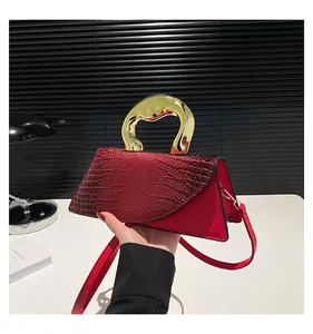 Detail of red crocodile texture handbag with unique sculptural gold metal handle