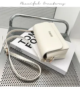 Close-up of cream white PU leather shoulder bag with gold metal buckle on a white book