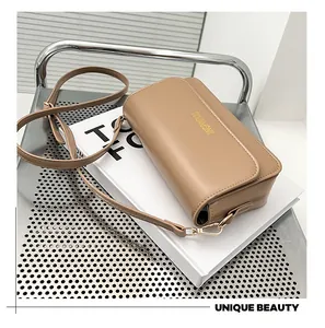 Close-up of khaki retro crossbody bag with golden logo on white books and metal chair