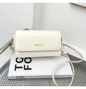 Detail of white PU leather flap bag with gold lettering on a minimalist white prop
