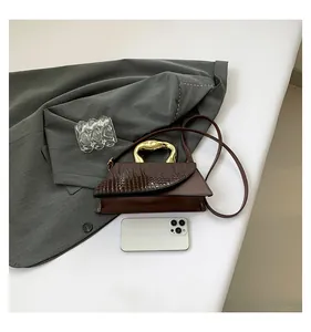 Detail of crocodile embossed flap and unique gold metal handle on dark brown handbag