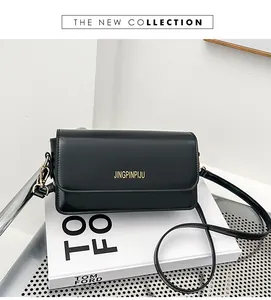 Detail of minimalist black faux leather crossbody bag with gold logo on a white book