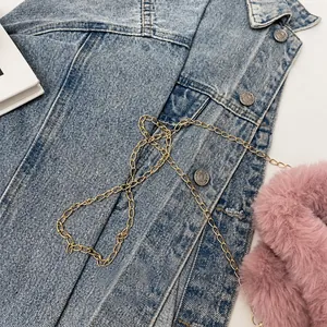 Detail of blue denim vest featuring metal buttons and decorative gold chain accessory
