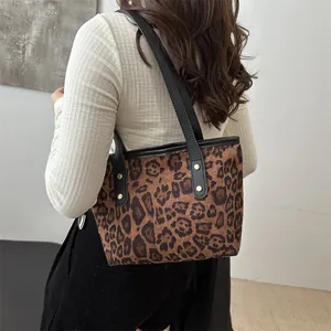 Detail of leopard print tote bag with black leather straps and gold rivet accents