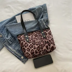 Detail of leopard print tote bag featuring black leather handles and gold metal rivets